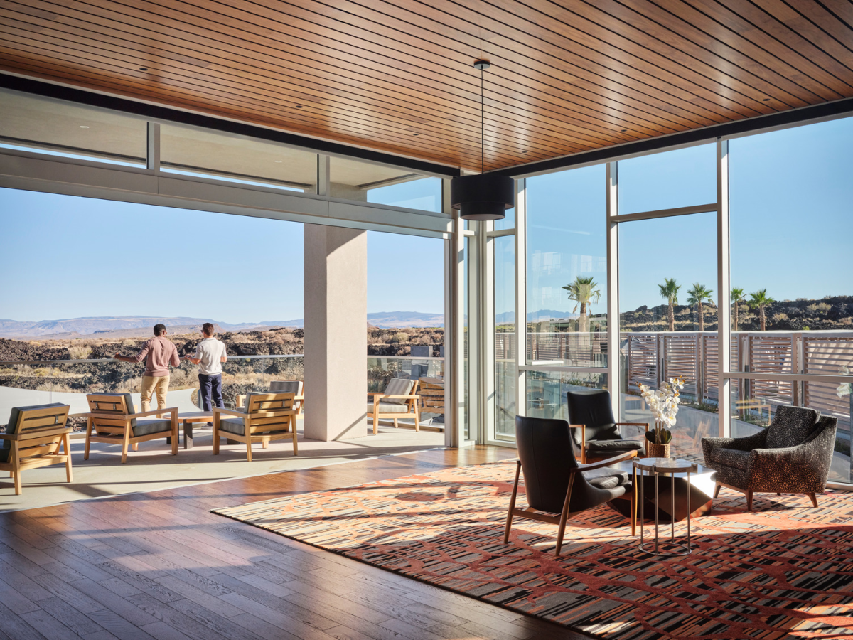 A sunny modern patio with glass doors, wooden ceiling, outdoor seating, and two men enjoying a desert view.