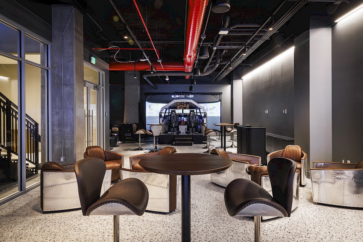 A sci‑fi control room with leather chairs, a central console, and exposed pipes and ducts along the ceiling.