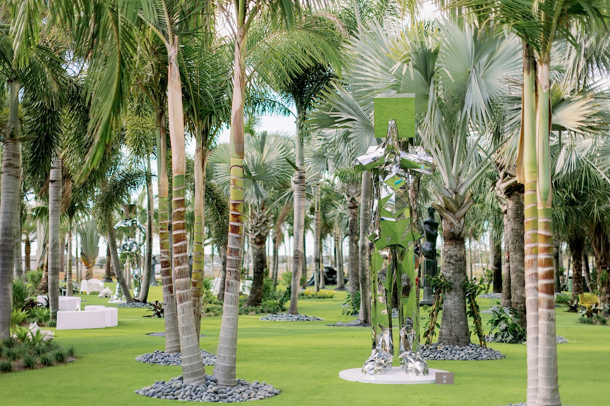 A tropical palm-filled garden event setup with greenery decor and a tall mirrored/green sculpture centerpiece.