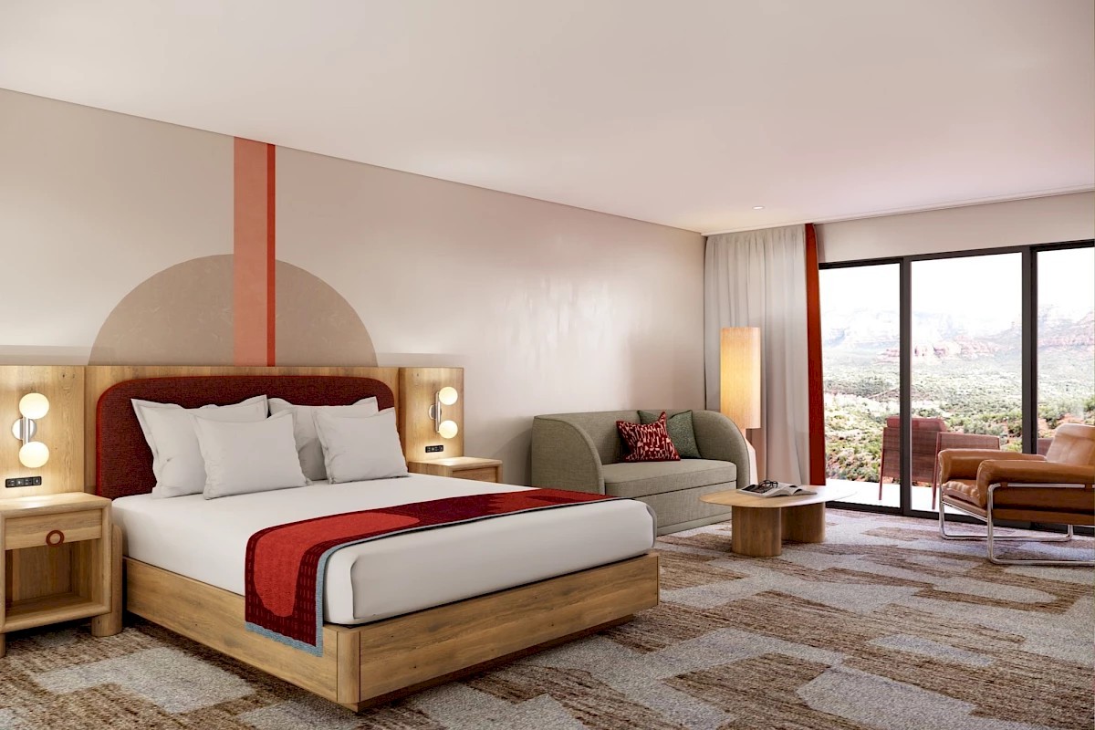 A modern hotel room with a king-sized bed, sitting area, rugs, and large window views of the landscape.