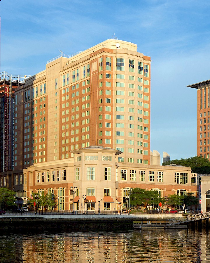 A riverfront view of downtown Boston’s World Trade Center area, with multiple brick office buildings rising against a clear blue sky.