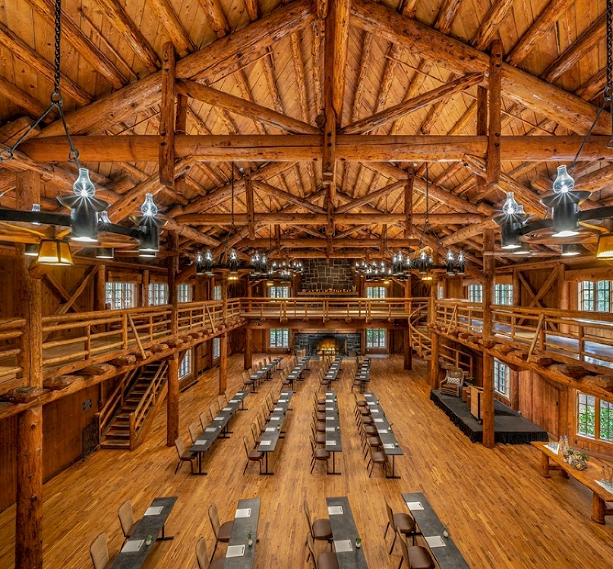 A spacious wooden hall with a vaulted timber ceiling, long banquet tables set in rows, and multiple hanging lamps.