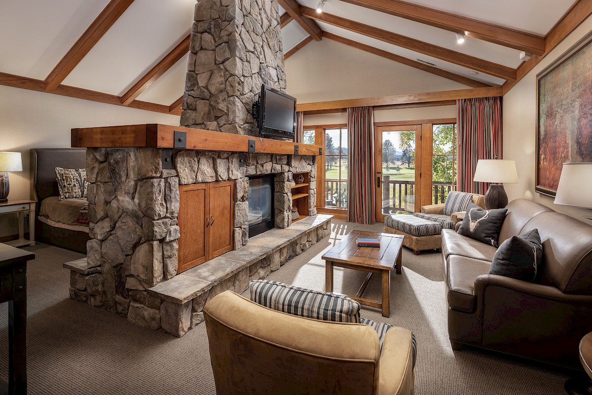 Cozy living room with a tall stone fireplace, mounted TV, wood beams, and striped curtains beside a sofa and coffee table.