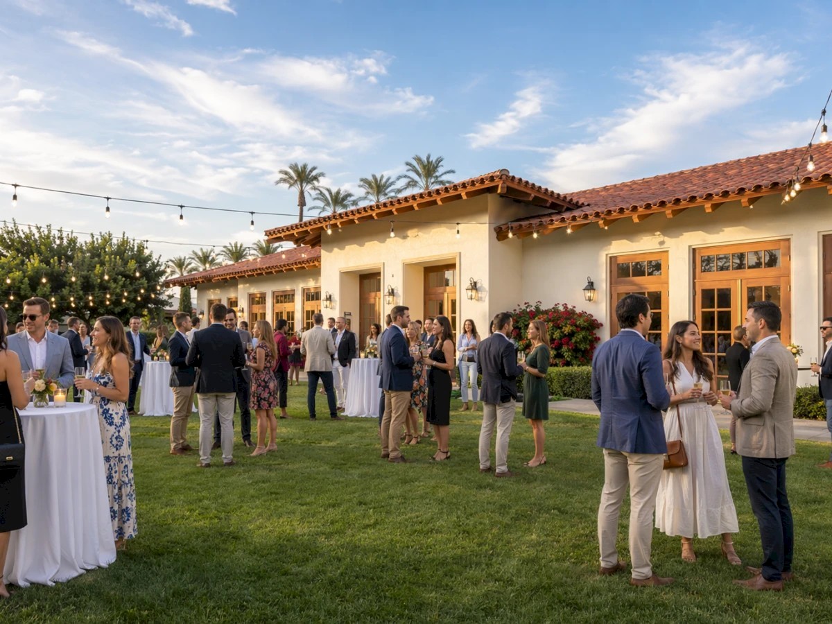 An outdoor wedding reception on a grassy lawn with guests mingling beside a decorated white building under string lights.