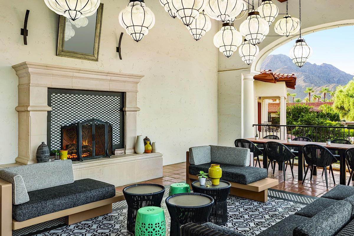 A luxurious patio lounge with a stone fireplace, hanging lanterns, gray cushioned seating, and a mountain view beyond.